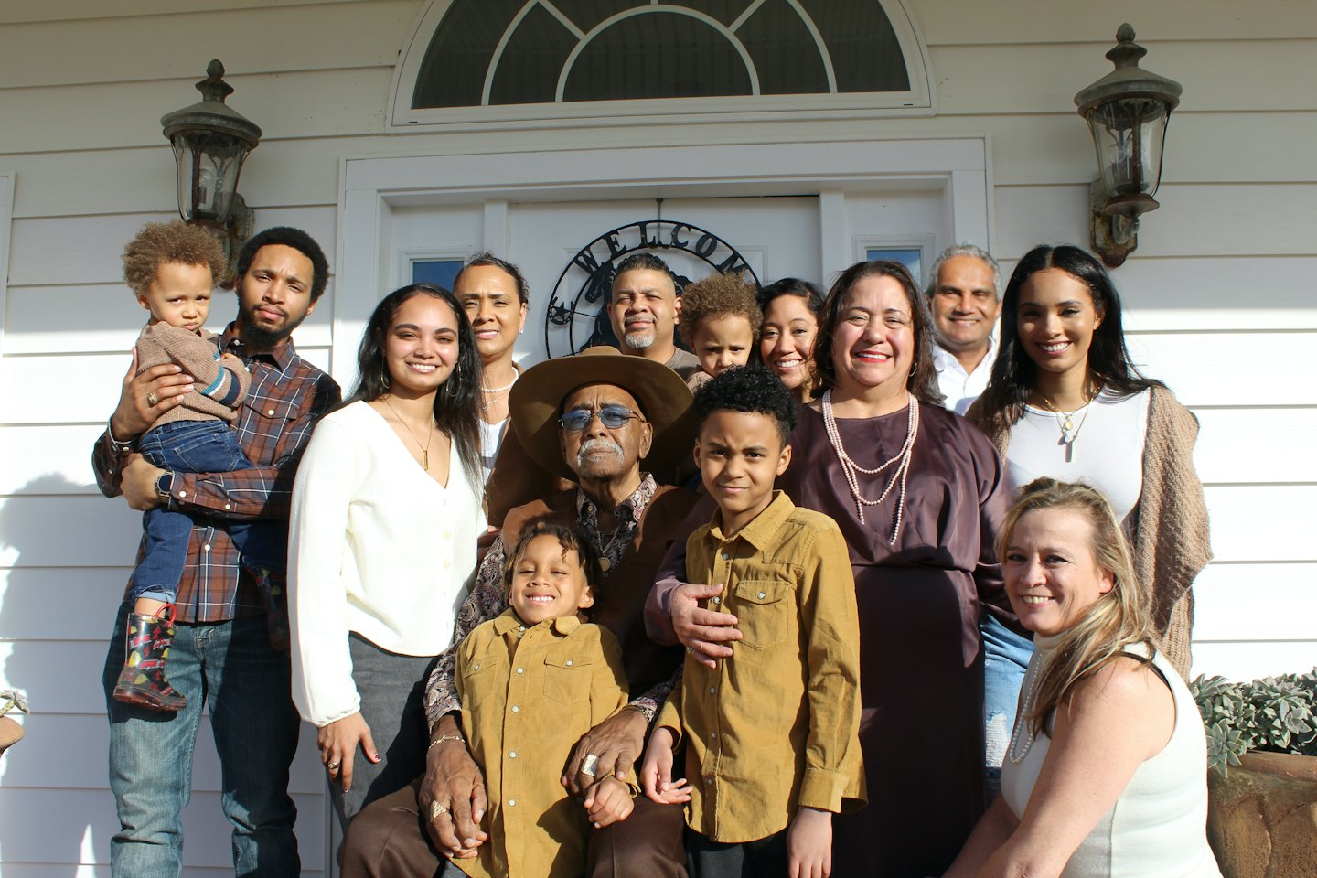 Multi-generational family smiles for a portrait outside a white house.